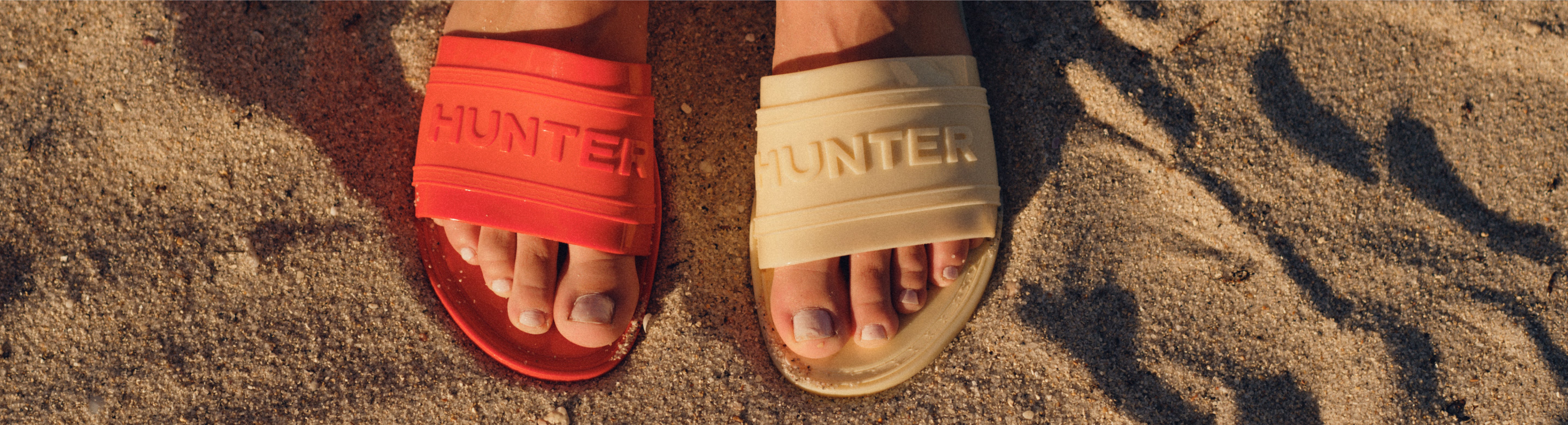 Model wearing Hunter slides in red and yellow on sand